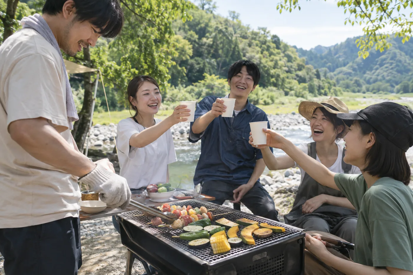川辺のバーベキューで乾杯する仲間たち